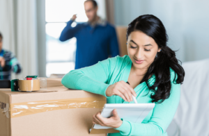 Woman holding a notepad and pen while leaning on a packing box with family in the background